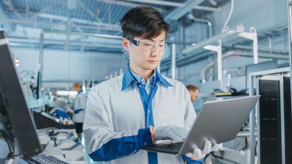 A technician in a laboratory setting working on a laptop 