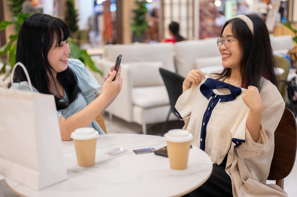 Two young customers smiling about their newly-purchased clothes in a coffee shop